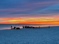 beach chairs on a sandy beach in a circle around a bonfire pit with an active sunsetting over the water