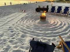 beach chairs on a sandy beach in a circle around an active bonfire with circles drawn in the sand around the bonfire pit