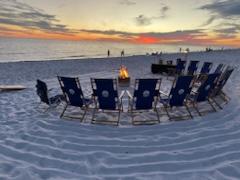 beach chairs on a sandy beach in a circle around an active bonfire over looking the suinset on the beach