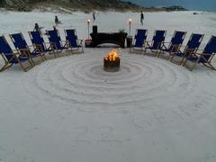 beach chairs on a sandy beach in a circle around an active bonfire