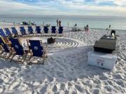 Photo of beach chiars in a half circle on a sandy beach with a fire pit in the middle with the water off in the background.