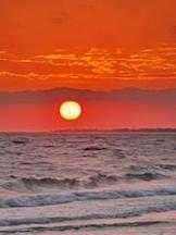 Sun setting just above the wavy ocean shore with a red orange colored sky.