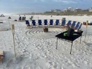 Photo of beach chiars in a half circle on a sandy beach with a fire pit in the middle with the trees off in the background.