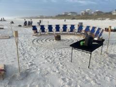 beach chairs on a sandy beach in a circle around a bonfire pit with tiki torches 