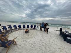 beach chairs on a sandy beach in a circle around a bonfire pit, dark cluds in the background over the water