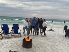 people standing within the circle of an active bonfire pit with the ocean in the background